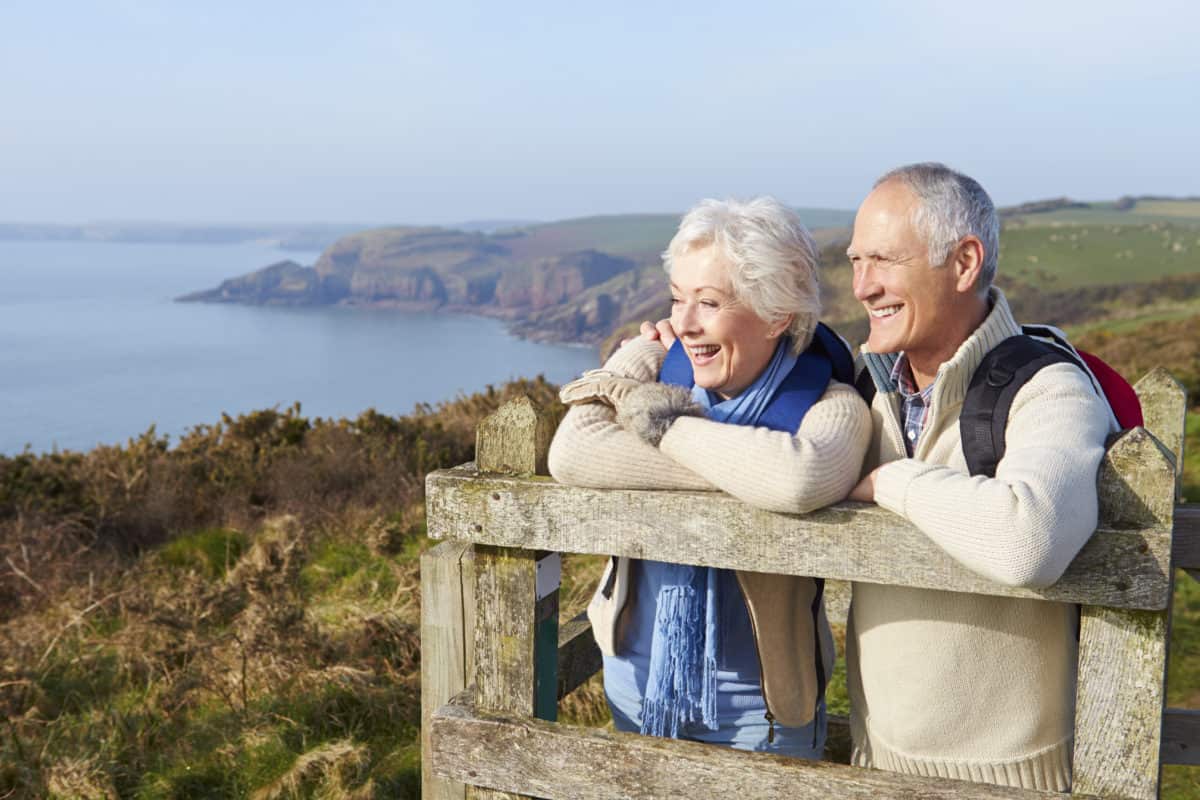 Senior couple enjoying a picturesque coastal view while leaning on a wooden fence, sharing a moment of joy and tranquility in nature.