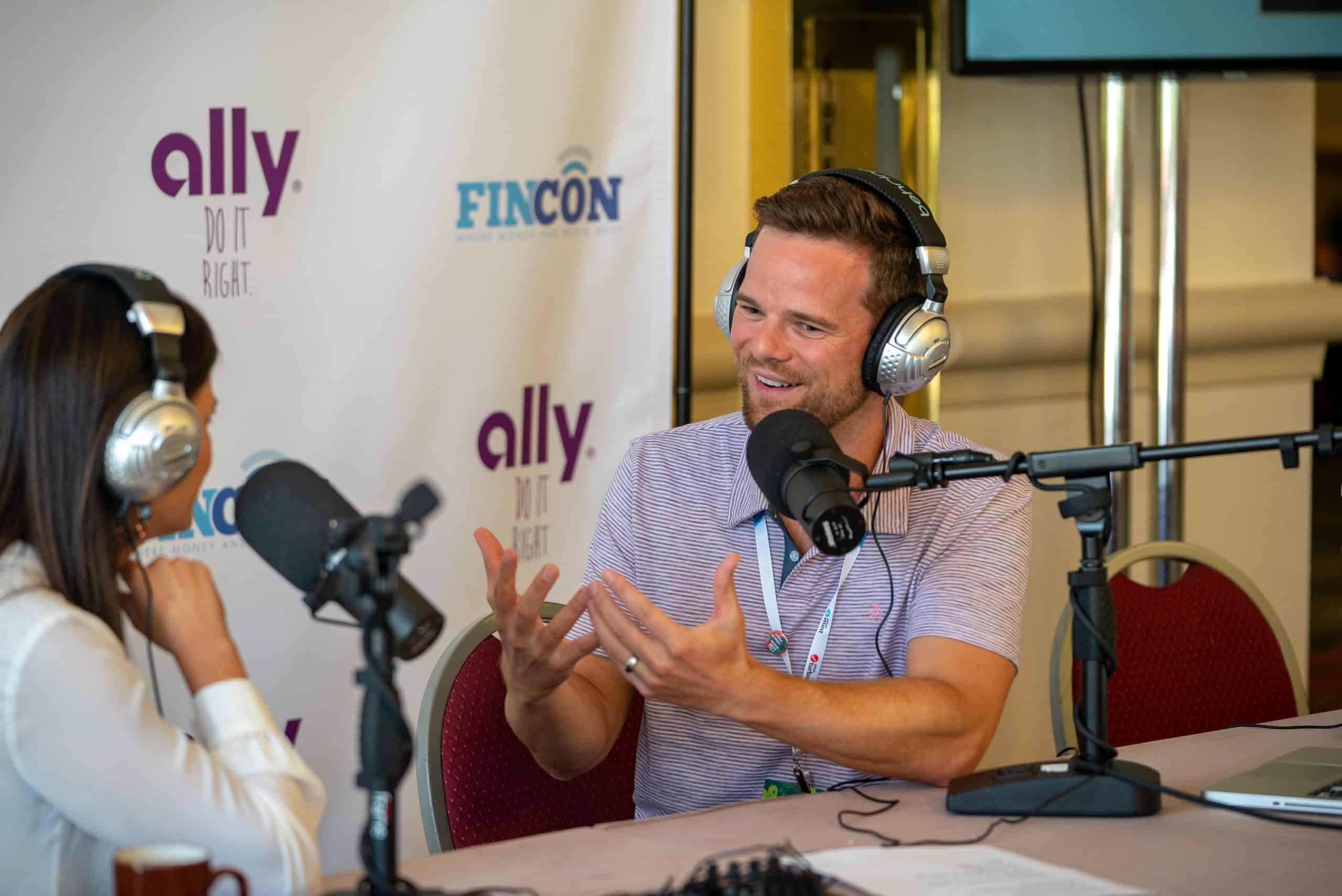 Two podcasters engaged in an animated conversation during a live recording session at a conference event.