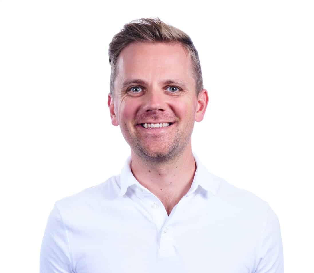 A smiling man with short hair wearing a white button-up shirt against a white background.