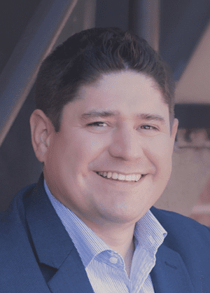 Smiling man in a professional blue suit and dress shirt confidently posing for a portrait.