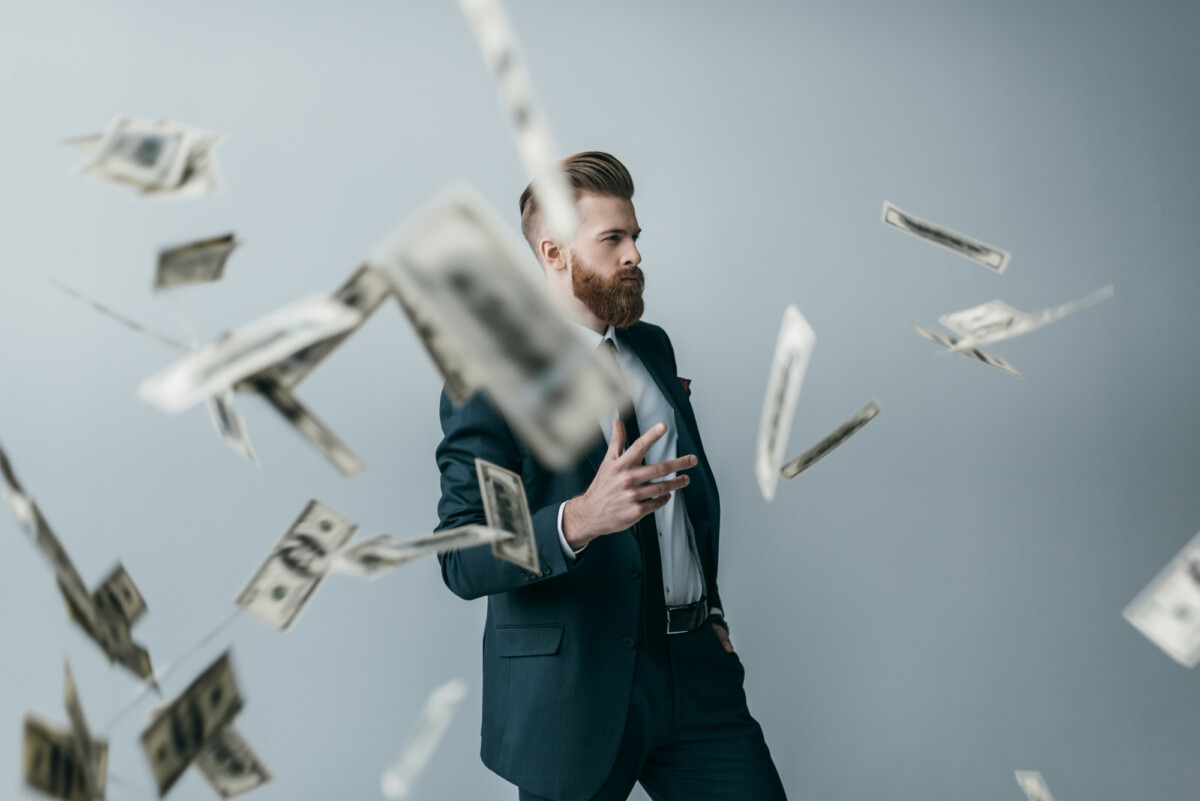 A man with a beard throwing dollar bills in the air.