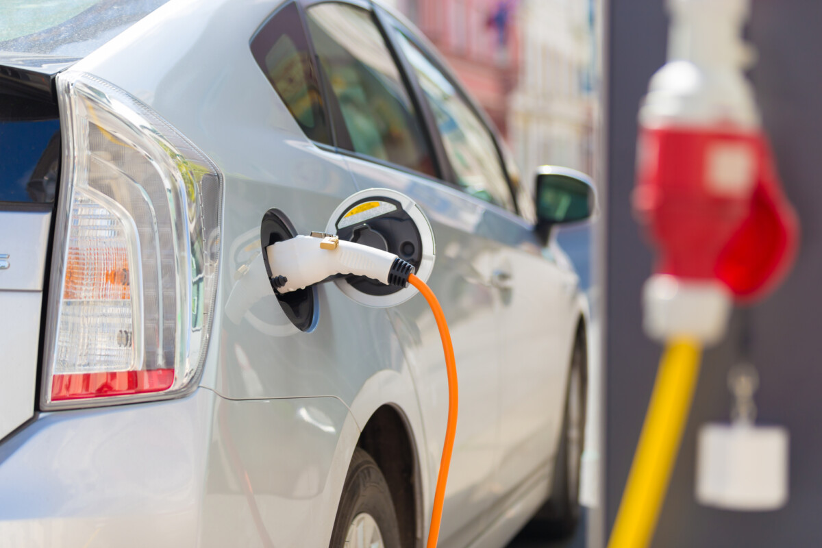 An electric vehicle being charged at a charging station with a vibrant orange cable.